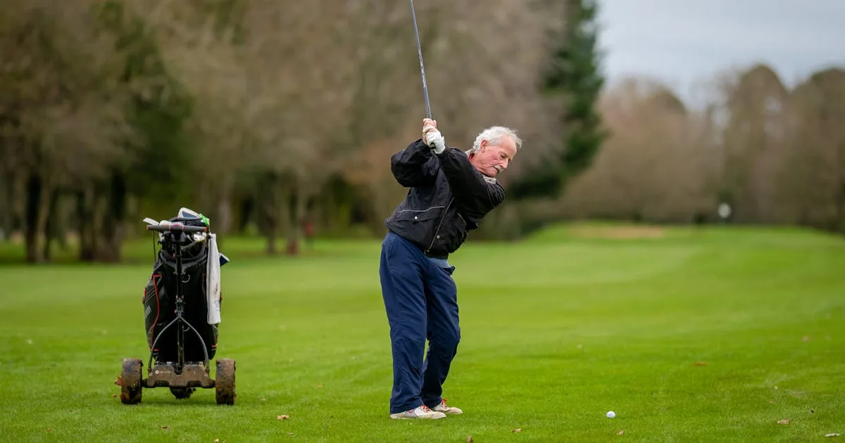 An elderly gentleman swinging a golf club on a vibrant green course