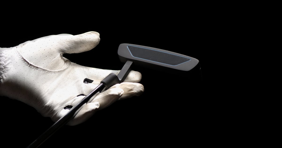 A close-up of a golf putter held by a gloved hand