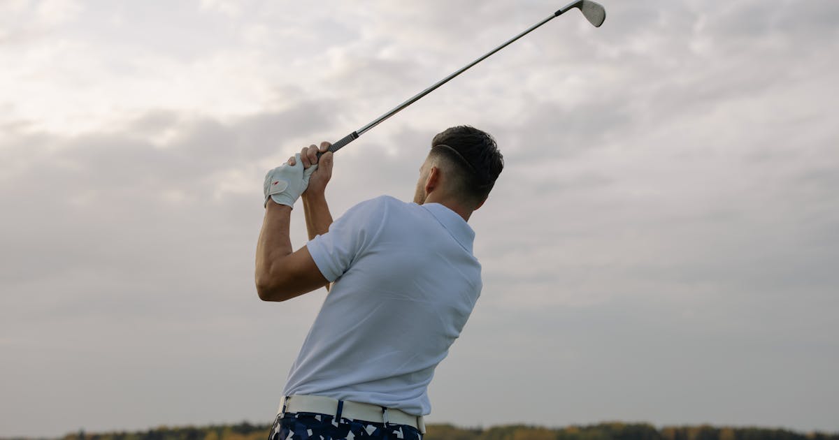 A golfer swinging a club outdoors on a cloudy day