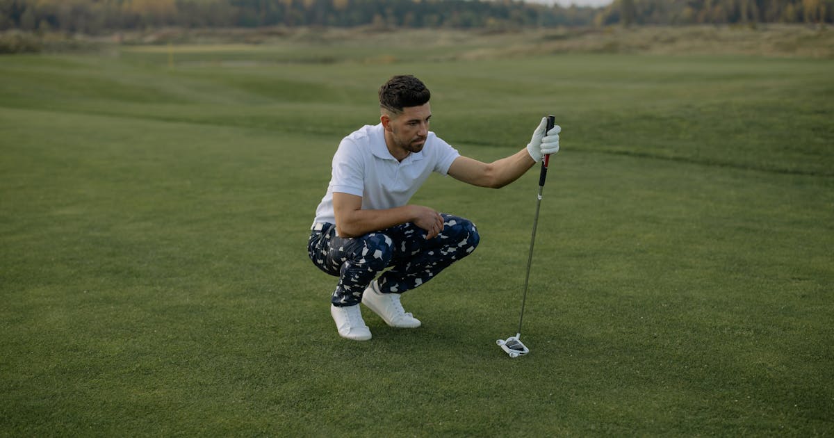 A golfer kneeling on a green course, preparing to putt